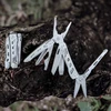 Pince multifonction NexTool dépliée sur une bûche en bois, outil de survie et camping en plein air.