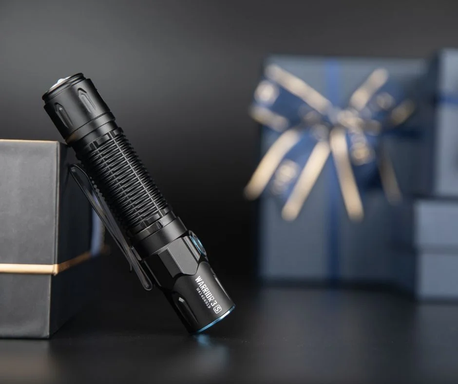 Torche tactique noire Warrior 3 S posée sur boîte, cadeaux flous en fond.