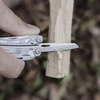 Couteau de poche d'un outil multifonction sculptant une branche de bois en plein air.