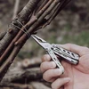 Pince d'un outil multifonction NexTool serrant un fil métallique autour de branches de bois en extérieur.