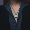 Un collier élégant avec un pendentif blanc et un insigne bleu, porté sur une chemise déboutonnée foncée.
