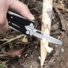 Couteau multifonction NexTool W40 sculptant une branche en bois pour le camping et la survie.