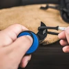 Mains nouant un paracorde noir et blanc sur un mini couteau croissant noir avec un anneau bleu texturé.