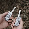 Deux pinces multifonctions de poche NexTool en acier inoxydable présentées en main sur fond de bois flouté.
