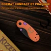 Couteau de poche pliant compact orange et violet Kizer édition Halloween avec manche ergonomique sur fond de bois sombre.