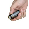 Olight Baton 4 gris en main, bouton doré et clip de poche pour un transport pratique.