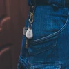 Porte-clés avec mousqueton doré, clés et balise Olight accrochés à la boucle de ceinture d'un jean bleu.